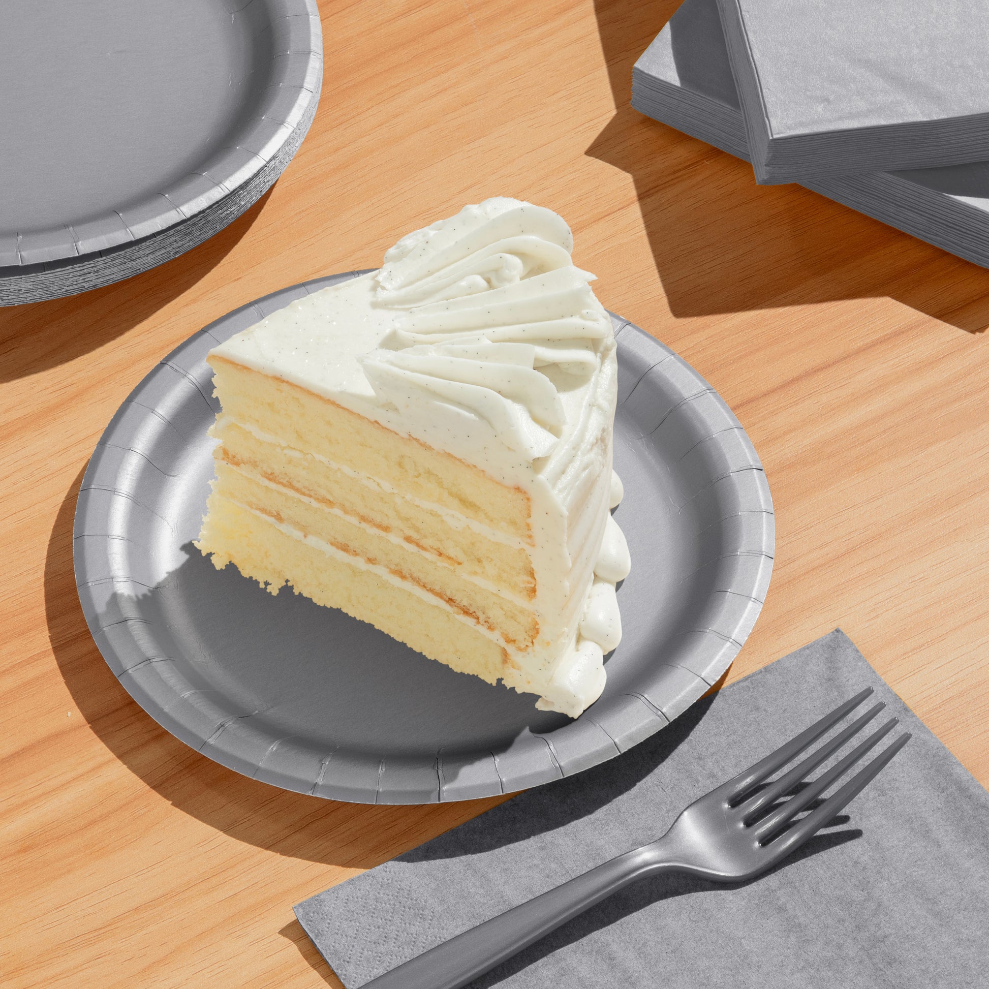 Slice of layered cake on a silver paper plate with a fork and napkin on a wooden table.